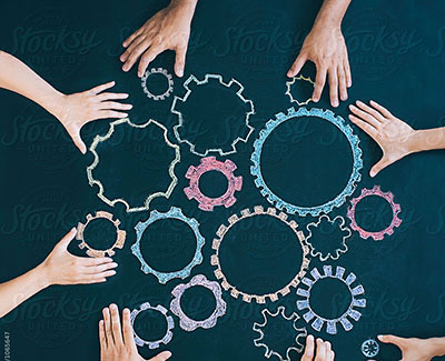 A photo of eight hands moving various coloured and sized cogs around on a blue background
